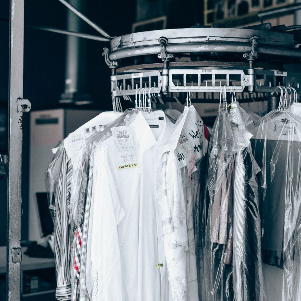 Clothes covered in plastic hanging from a rotating dry cleaning conveyor system at a dry cleaners. Image for About Rochelle Cleaners.